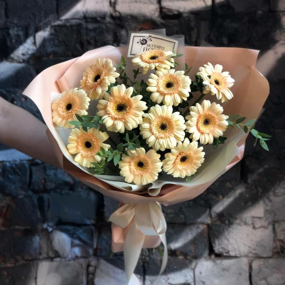 Букет из 11 персиковых мини-гербер и зелени в дизайнерской упаковке 